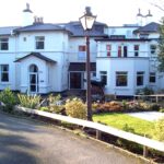 A large, white house with multiple storeys and a welcoming garden at the front serves as an inviting Wirral care home. There’s a lamp post and path leading gracefully to the entrance, embodying the warmth and community spirit of Abbeyfield.