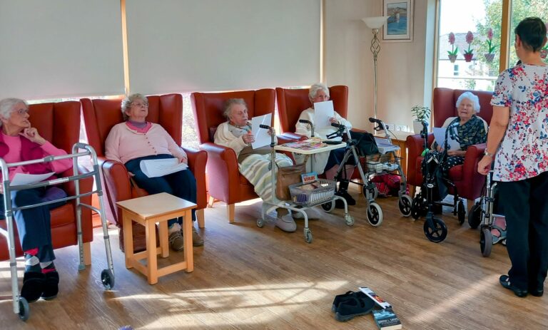 A group of elderly women are seated comfortably in chairs at the Abbeyfield Wirral Care Home, enjoying restful moments of camaraderie and companionship.