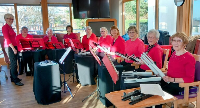 In a cosy room at the residential care home, eleven people in red tops sit among hand chimes and music stands, preparing for a charming musical performance.