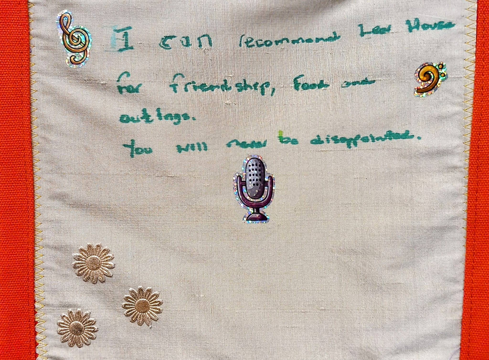 Handwritten text on fabric reads, I can recommend Lost Houses for friendship, food, and outings. You will not be disappointed. Decorated with musical notes, flowers, and a microphone sticker, it evokes the warmth of a welcoming care home in Wirral.