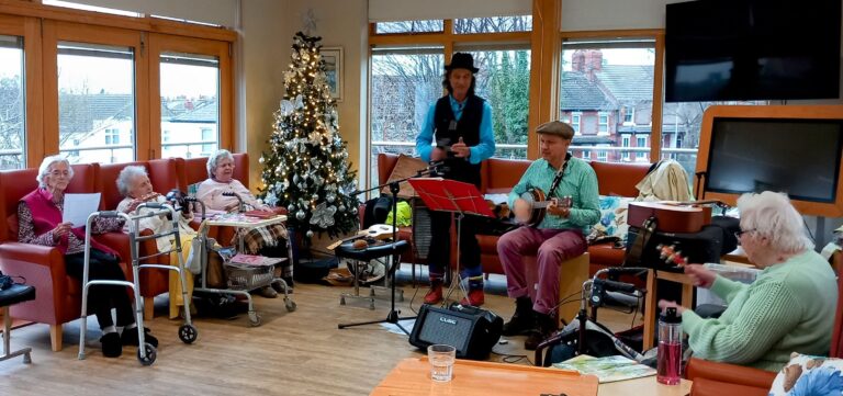 A group of elderly people sit and play musical instruments in a room adorned with a Christmas tree and lights, bringing festive cheer to the residential care home.